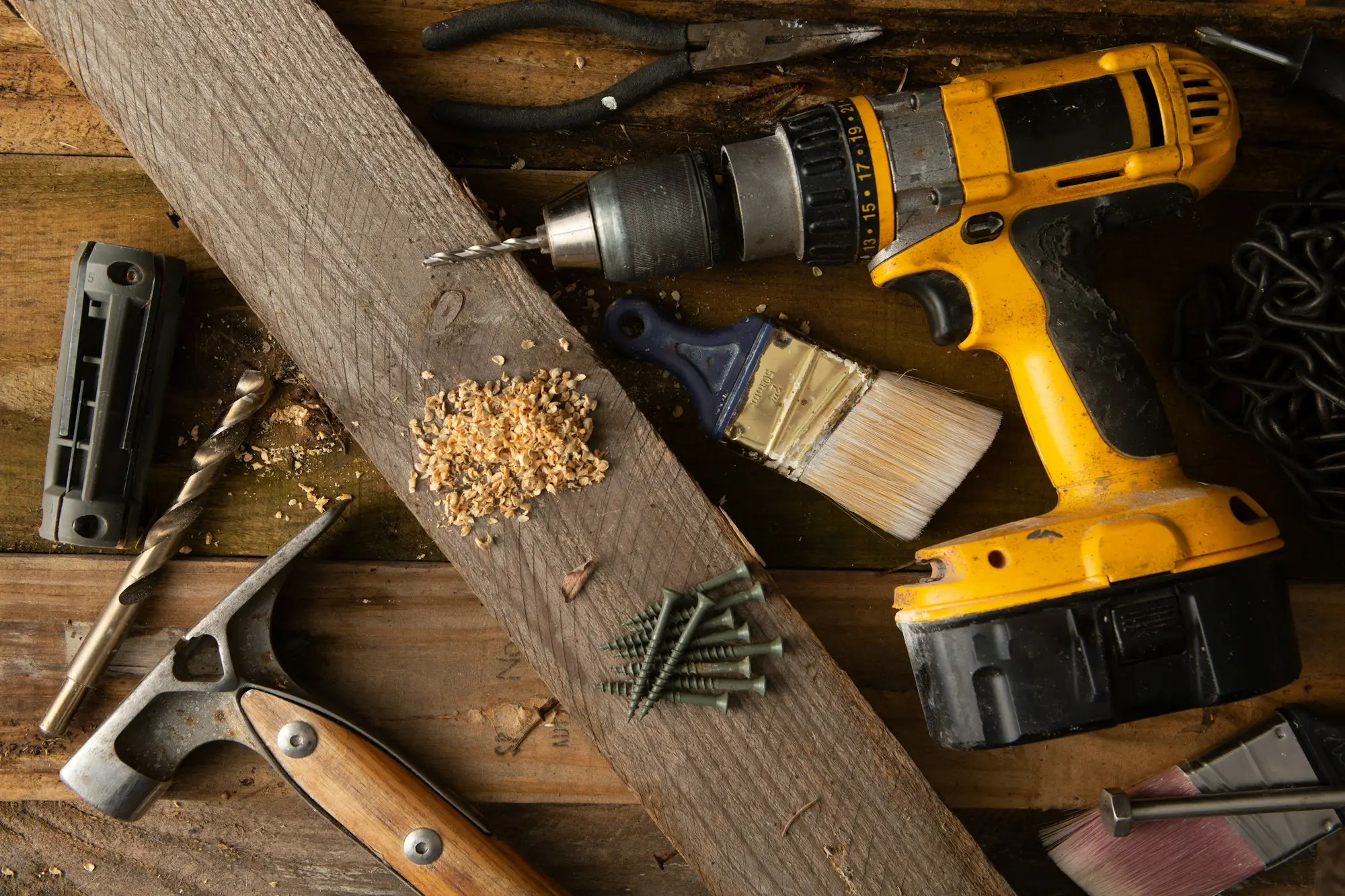 Cordless drill, hammer, screws, sawdust and a paintbrush on a timber board, the tools of a trades business setting deposit and payment terms